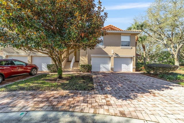 view of front facade with a garage, decorative driveway, a tile roof, and stucco siding