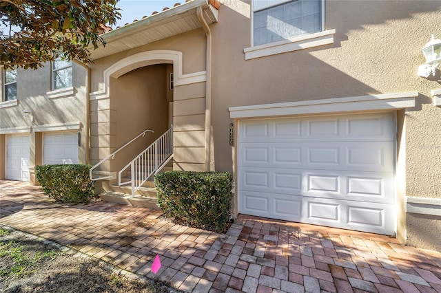 property entrance featuring a garage, decorative driveway, and stucco siding