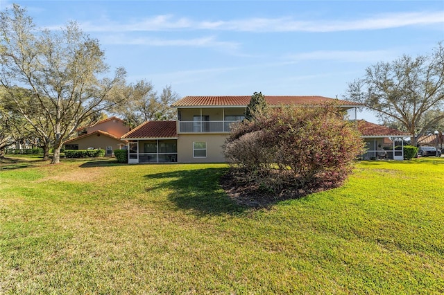 rear view of house with a sunroom, a lawn, a balcony, and stucco siding