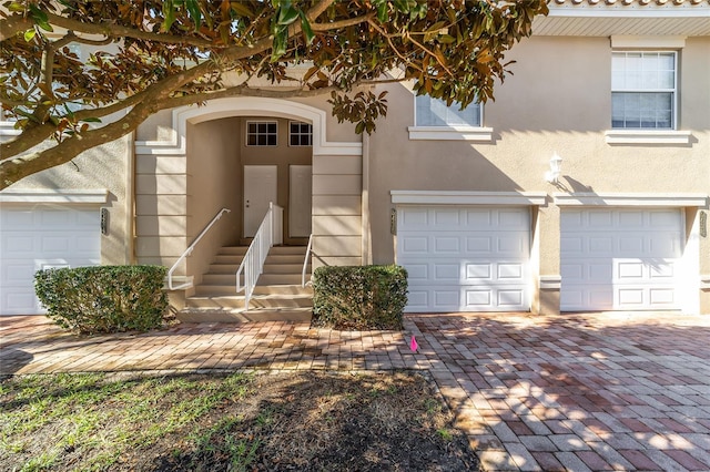 doorway to property with a garage, decorative driveway, and stucco siding