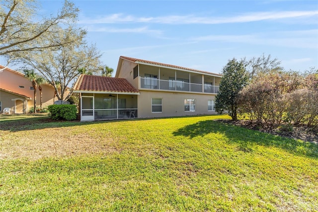 back of house featuring a balcony, a sunroom, a ceiling fan, and a lawn