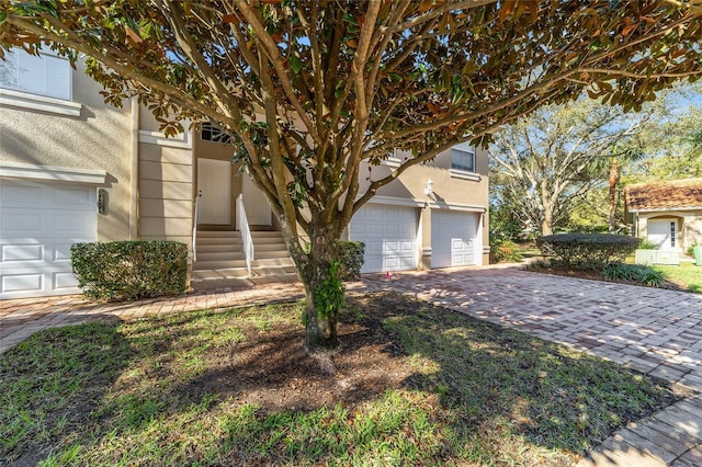 view of property hidden behind natural elements featuring a garage, entry steps, decorative driveway, and stucco siding