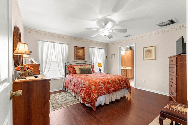 bedroom featuring dark wood-style flooring, visible vents, ensuite bath, and baseboards