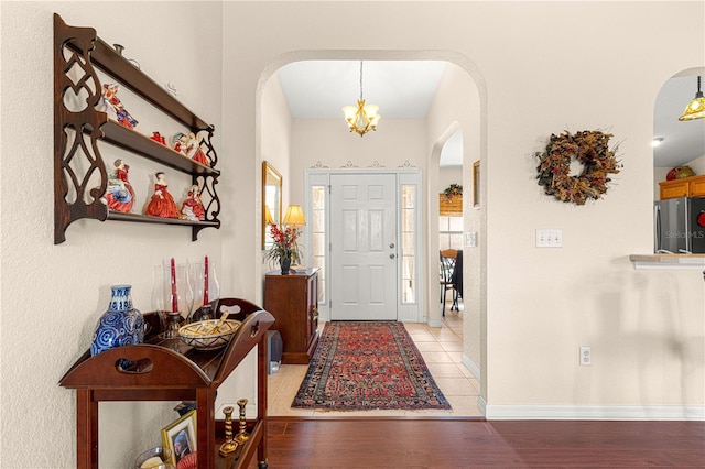 entrance foyer featuring light wood-type flooring, an inviting chandelier, baseboards, and arched walkways