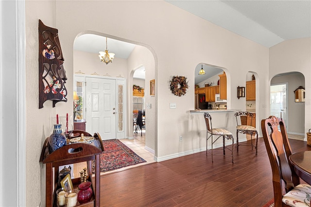 foyer featuring lofted ceiling, baseboards, arched walkways, and wood finished floors