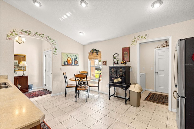 dining area featuring arched walkways, vaulted ceiling, a textured ceiling, and light tile patterned floors