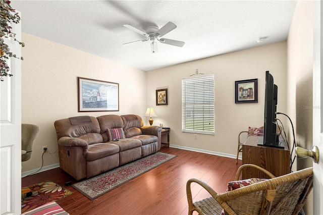 living room featuring wood-type flooring, baseboards, ceiling fan, and a textured ceiling