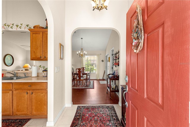 foyer with arched walkways, light tile patterned flooring, a notable chandelier, and baseboards