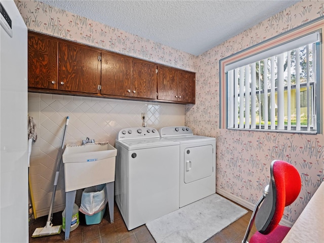 clothes washing area with a textured ceiling, baseboards, cabinet space, washing machine and clothes dryer, and wallpapered walls