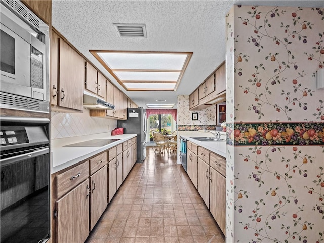 kitchen with visible vents, under cabinet range hood, light countertops, black appliances, and a sink