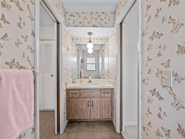 bathroom with wallpapered walls, baseboards, a closet, and vanity