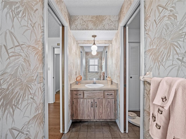 bathroom with a closet, a textured ceiling, vanity, baseboards, and wallpapered walls