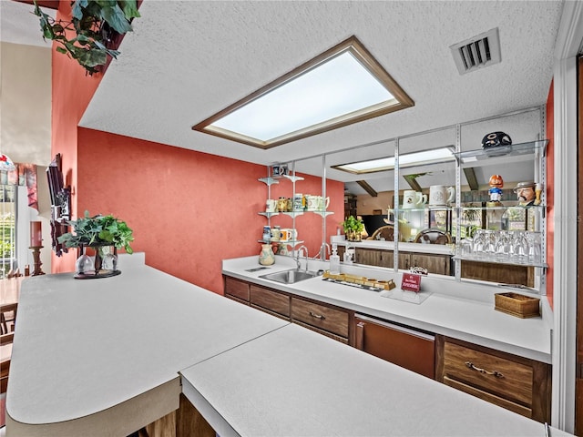 kitchen featuring a textured ceiling, brown cabinetry, a sink, and visible vents