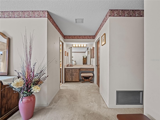 hallway with light colored carpet, visible vents, a textured ceiling, and baseboards