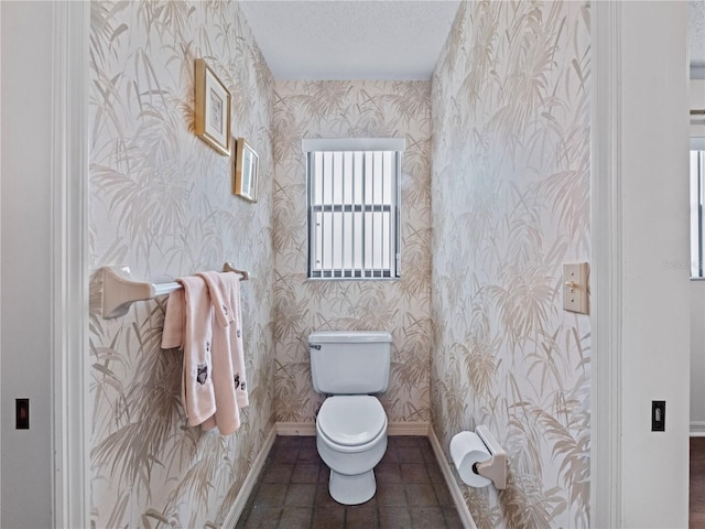 half bathroom featuring toilet, a textured ceiling, baseboards, and wallpapered walls