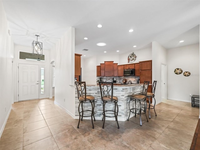 kitchen with arched walkways, a breakfast bar, decorative backsplash, brown cabinets, and stainless steel microwave