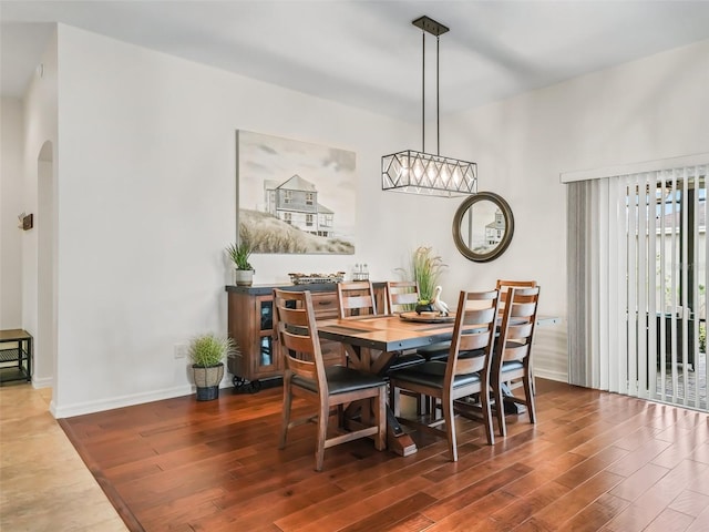 dining room with arched walkways, a notable chandelier, baseboards, and wood finished floors