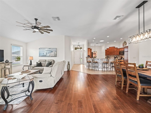 living area with dark wood-style floors, lofted ceiling, visible vents, and a ceiling fan