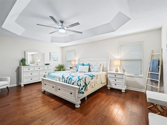 bedroom featuring ceiling fan, a tray ceiling, dark wood finished floors, and baseboards