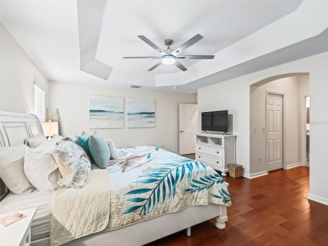 bedroom with arched walkways, wood finished floors, visible vents, baseboards, and a raised ceiling