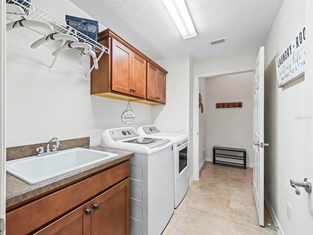 clothes washing area with cabinet space, visible vents, a textured ceiling, washing machine and dryer, and a sink