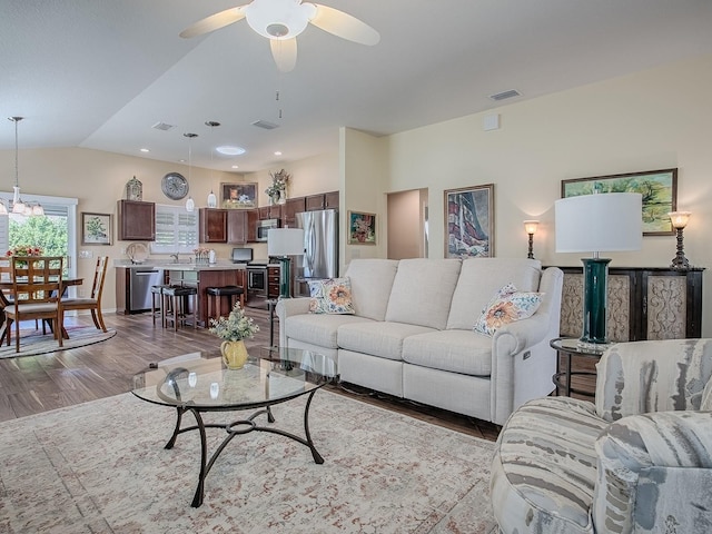 living area featuring a ceiling fan, lofted ceiling, visible vents, and wood finished floors