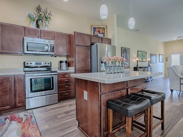 kitchen featuring a breakfast bar area, open floor plan, stainless steel appliances, light countertops, and light wood-style floors