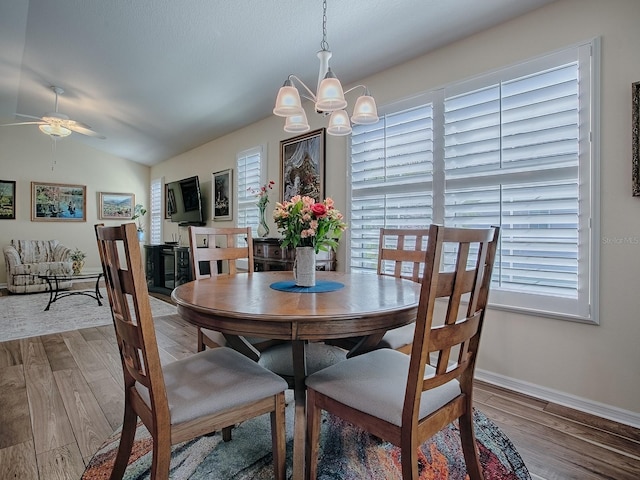 dining room featuring ceiling fan with notable chandelier, lofted ceiling, baseboards, and wood finished floors