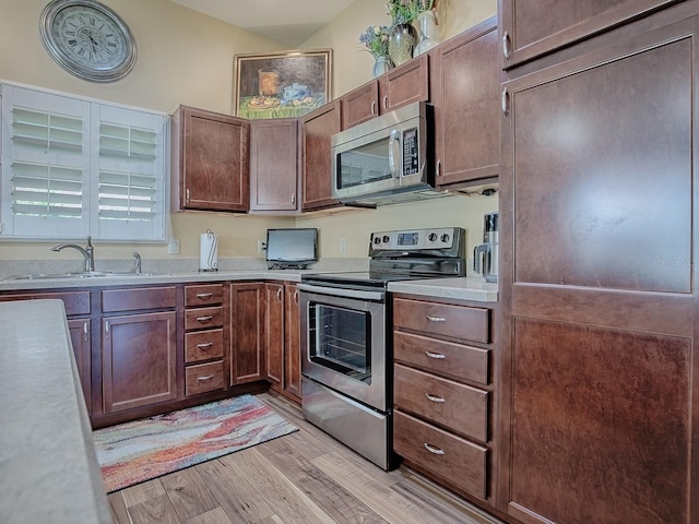 kitchen with stainless steel appliances, a sink, light countertops, and light wood-style floors