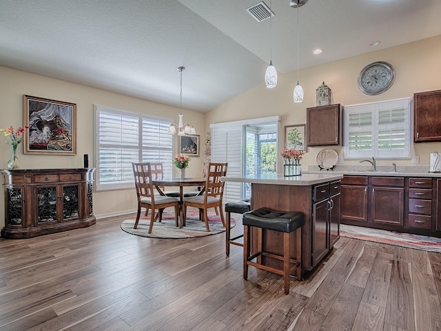 kitchen with visible vents, wood finished floors, a center island, vaulted ceiling, and light countertops