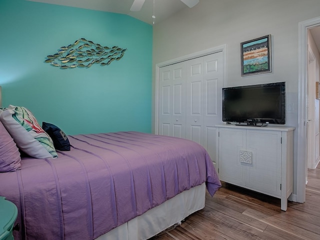 bedroom with lofted ceiling, a closet, wood finished floors, and a ceiling fan