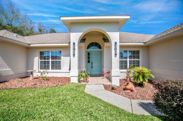 property entrance with a shingled roof, a lawn, and stucco siding