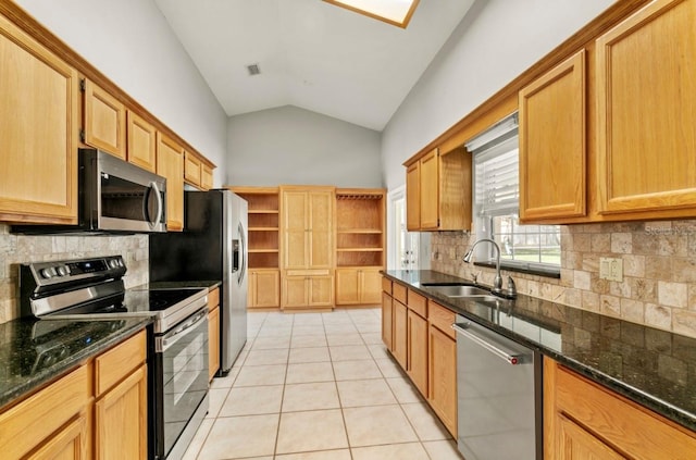 kitchen featuring stainless steel appliances, light tile patterned flooring, vaulted ceiling, a sink, and dark stone counters