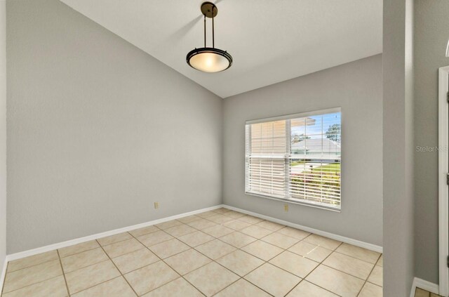 empty room featuring vaulted ceiling, light tile patterned flooring, and baseboards