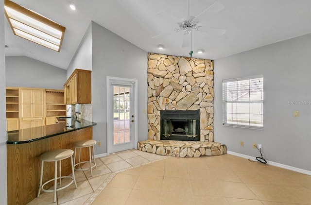 kitchen with light tile patterned flooring, a fireplace, a sink, lofted ceiling with skylight, and dark countertops