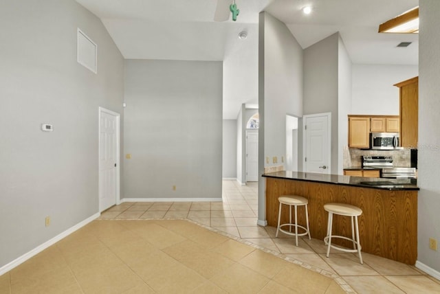 kitchen with dark countertops, high vaulted ceiling, stainless steel appliances, and light tile patterned flooring