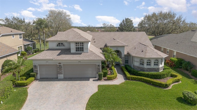 view of front of property with decorative driveway, roof with shingles, stucco siding, stone siding, and a front lawn