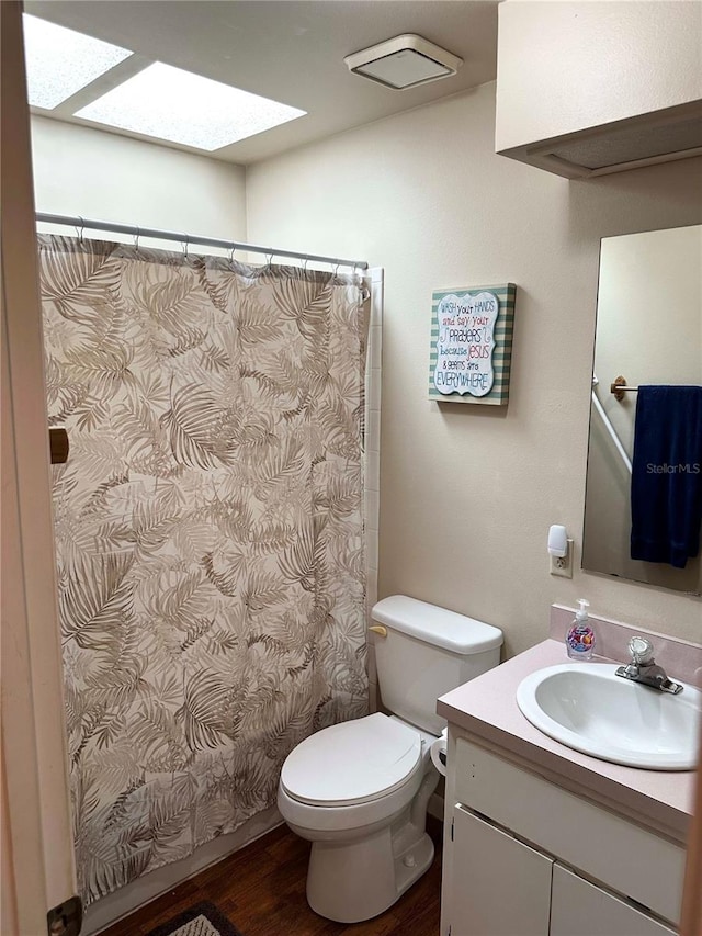 bathroom with toilet, a skylight, wood finished floors, vanity, and a shower with curtain