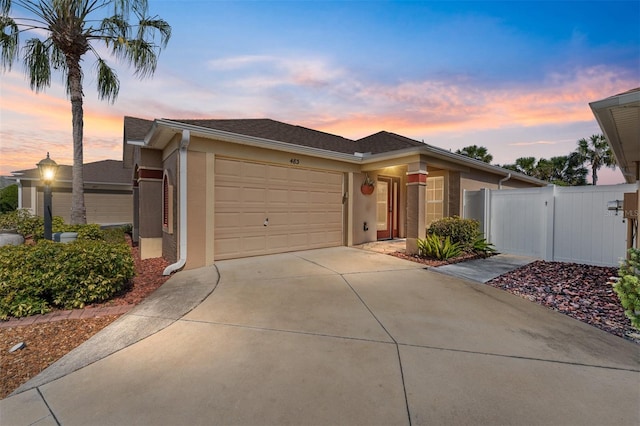 view of front of house featuring driveway, an attached garage, a gate, and stucco siding