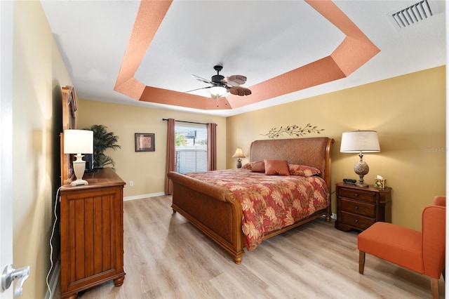 bedroom with light wood-style flooring, a ceiling fan, visible vents, baseboards, and a raised ceiling