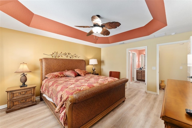 bedroom with visible vents, a raised ceiling, light wood-style flooring, and baseboards