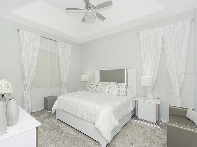 bedroom featuring light carpet, a raised ceiling, and a ceiling fan