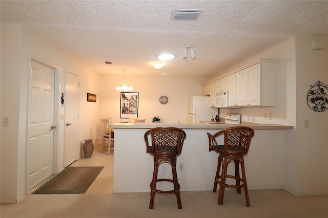 kitchen featuring a breakfast bar area, visible vents, white cabinetry, white appliances, and a peninsula