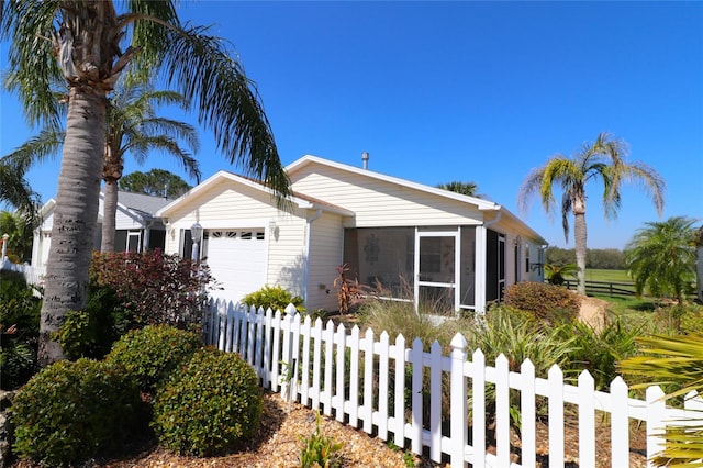 view of front of home with a fenced front yard, an attached garage, and a sunroom