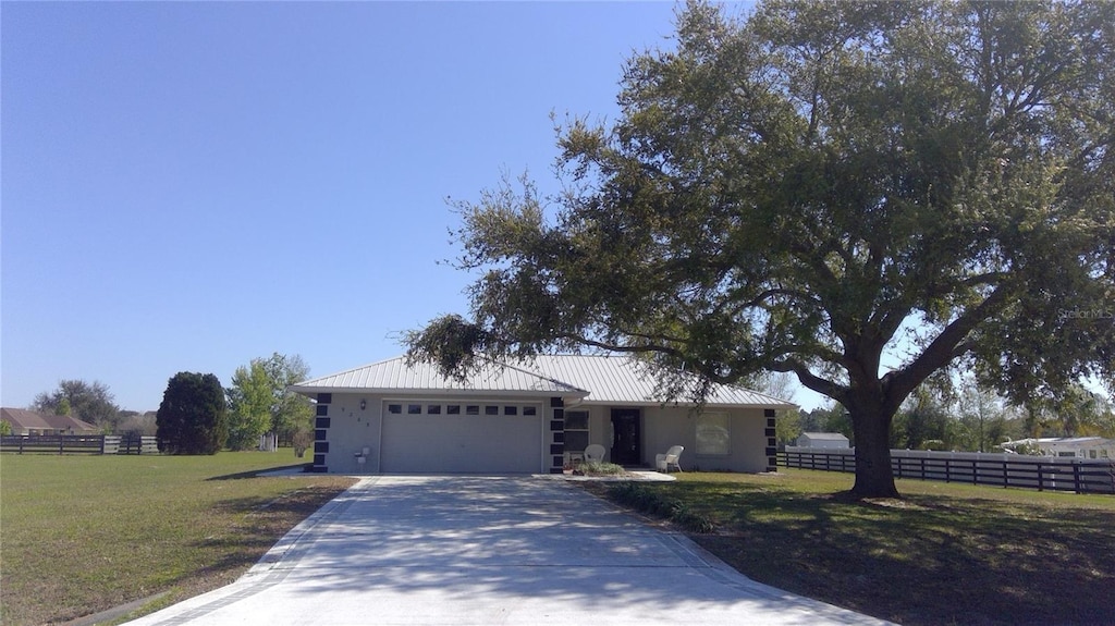 ranch-style home with metal roof, fence, a front lawn, and an attached garage