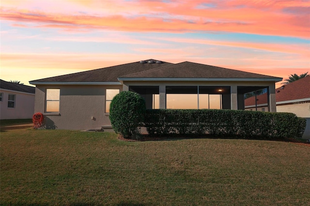 rear view of property featuring a sunroom, roof with shingles, a yard, and stucco siding