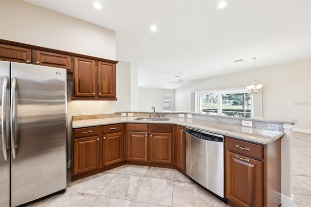 kitchen featuring light stone counters, a peninsula, a sink, appliances with stainless steel finishes, and brown cabinets