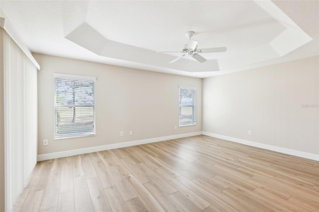 empty room featuring a ceiling fan, light wood-type flooring, a raised ceiling, and baseboards