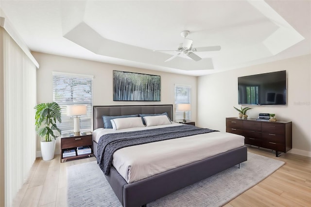 bedroom featuring light wood finished floors, multiple windows, and a tray ceiling