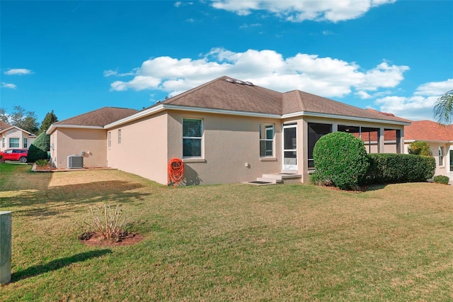 rear view of property with a sunroom, central AC unit, a lawn, and stucco siding